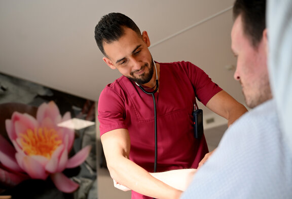 Pflegefachkräfte steht vor einem Patienten und hört mit einem Stethoskop den Patienten ab.